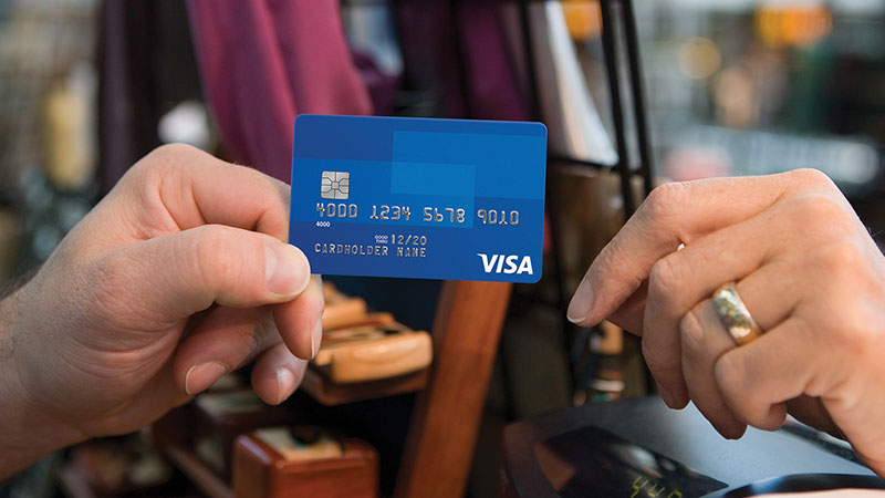 An Image of two individuals where one person hands a Visa credit card to another.